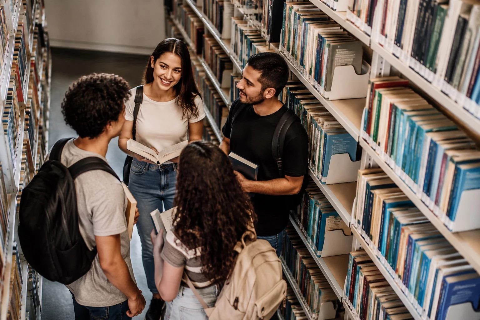 Estudantes conversando em pé entre as estantes de uma biblioteca